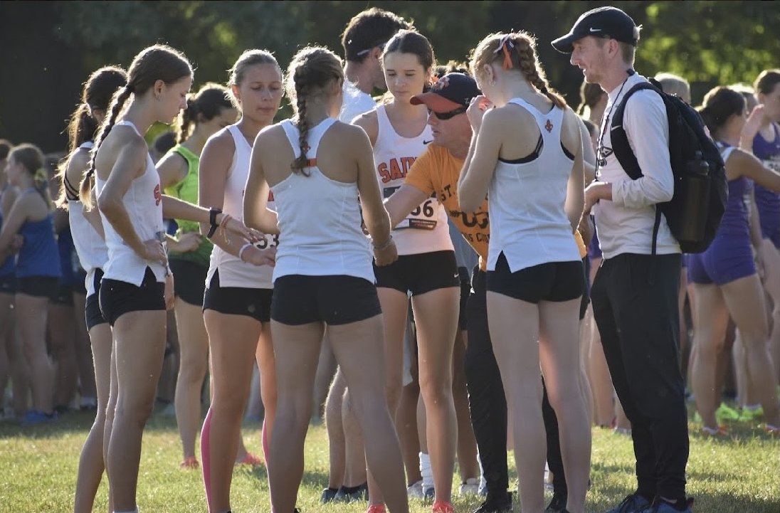 Girls' cross country runners gather around couches Bradley Kaplan (left) and Brandon Wilkerson (right) for team huddle. Photo by Angie Kreeger.
