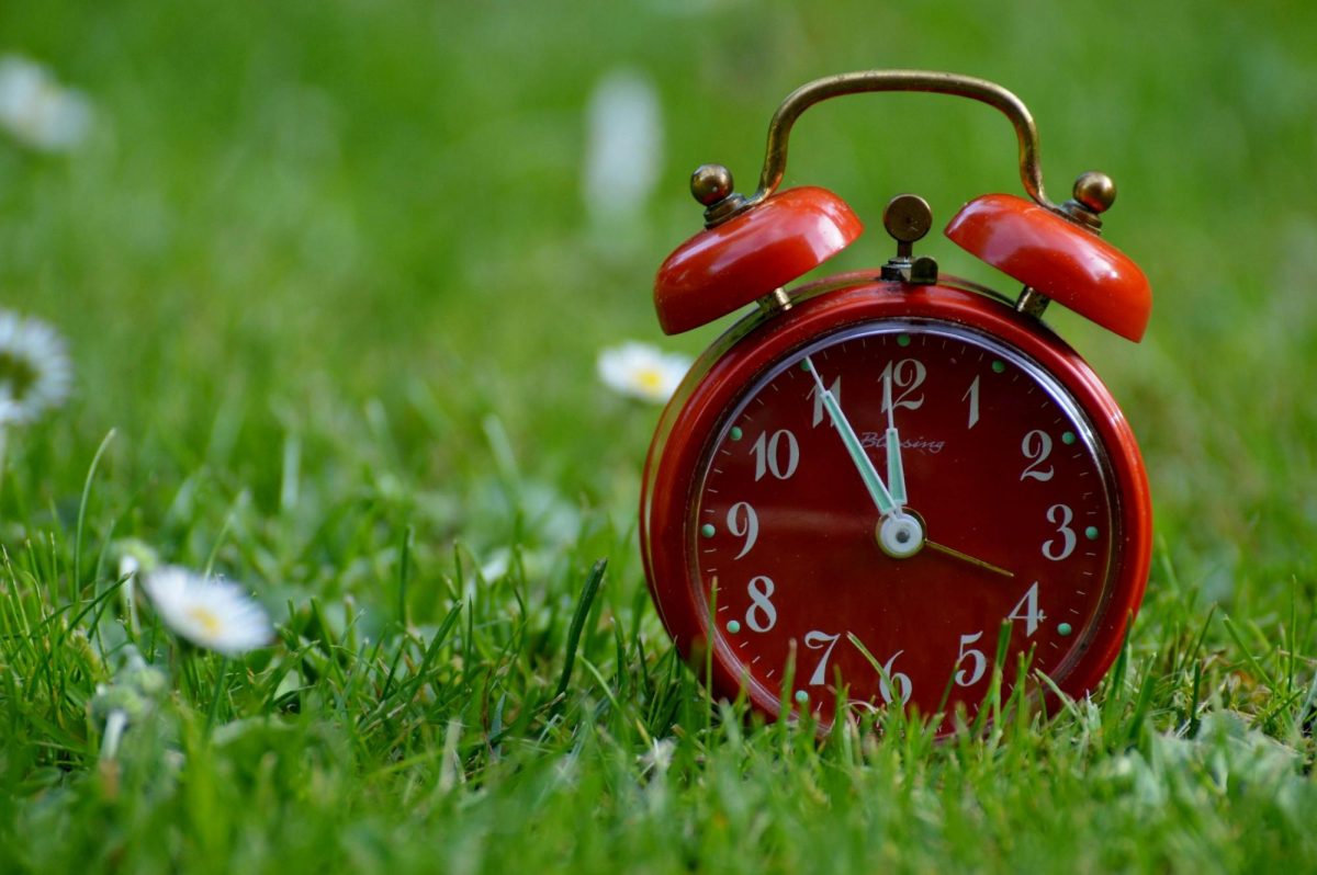 A red alarm clock rests on a field of grass. Photo courtesy of Pexels.
